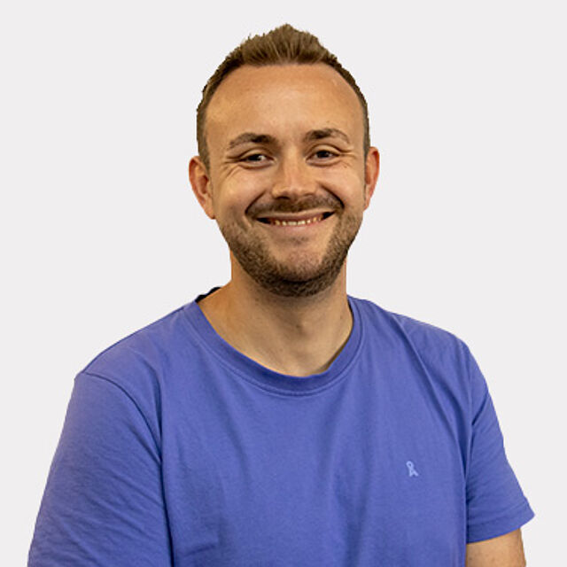 Mann mit braunen Haaren und blauem T-Shirt vor weißem Hintergrund