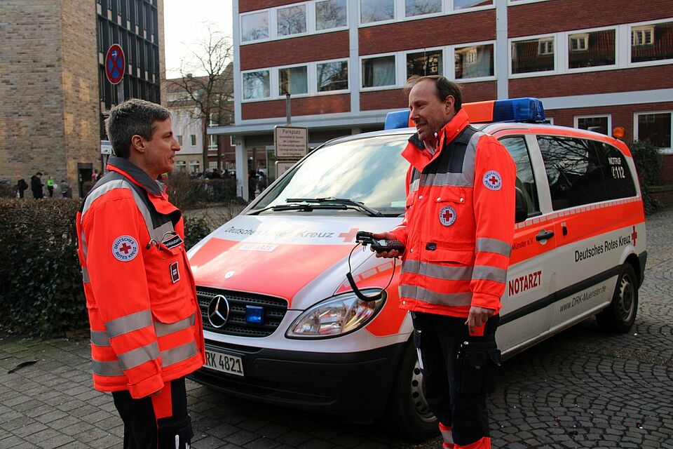 NEF Zwei Männer in Einsatzkleidung vor dem Notarzteinsatzfahrzeug