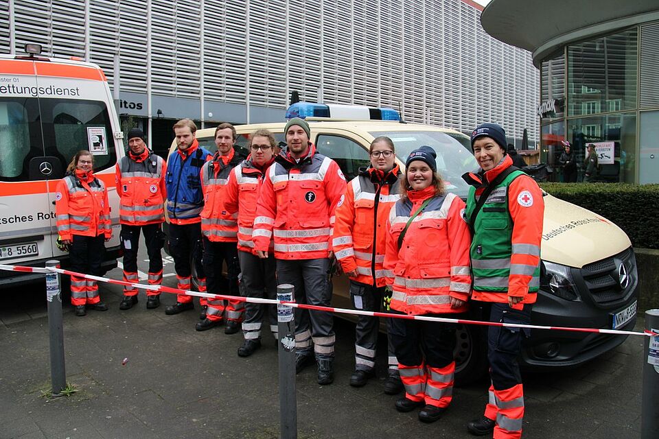 Rosenmontag Neun Personen in Einsatzkleidung vor zwei Einsatzfahrzeugen. Im Hintergrund moderne Gebäude.