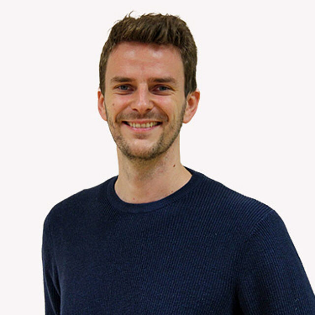 Mann mit braunen Haaren und blauem Pullover vor weißem Hintergrund