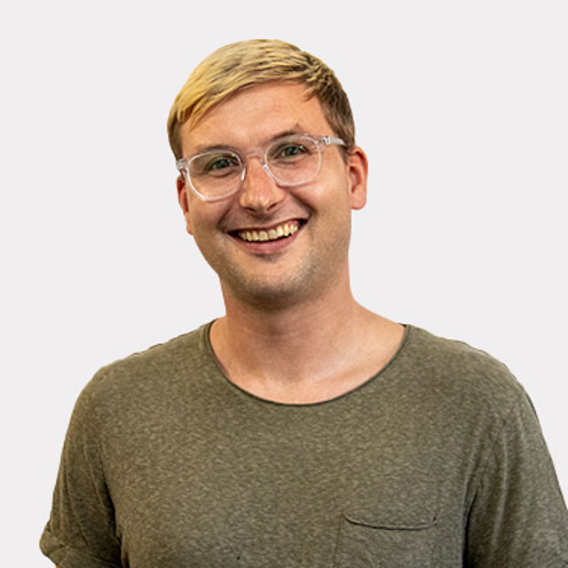Mann mit Brille und grünem Oberteil vor weißem Hintergrund