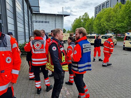 Mehrere Personen in Einsatzkleidung stehen beisammen, im Hintergrund eine Halle und Fahrzeuge