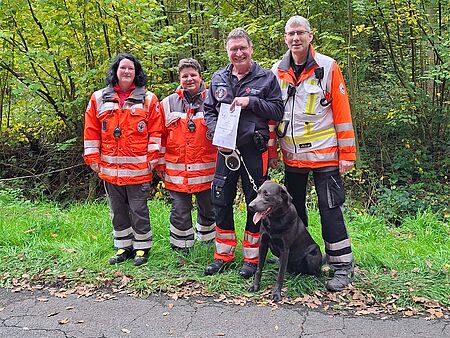 4 Personen in Einsatzbekleidung mit einem Rettungshund