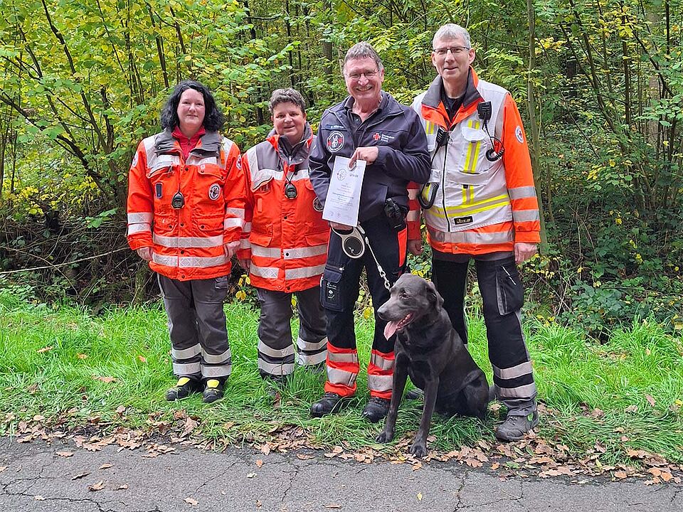 4 Personen in Einsatzbekleidung mit einem Rettungshund