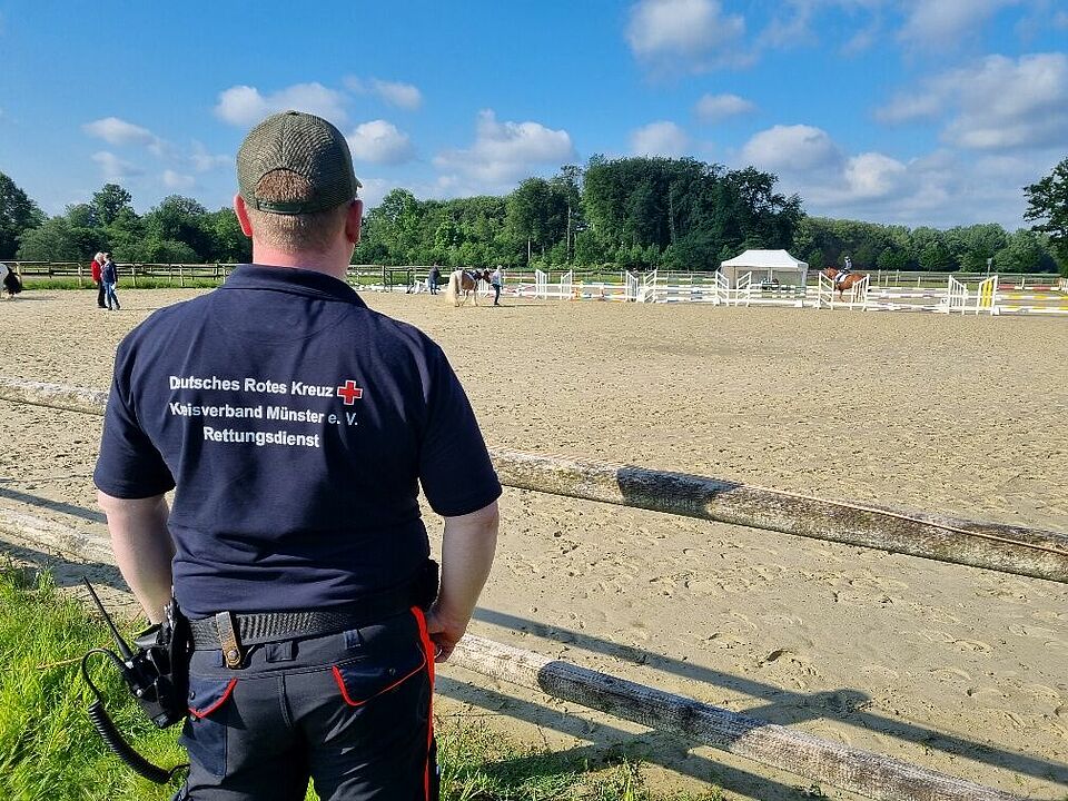Reitplatz Eine Person in Einsatzkleidung von hinten fotografiert vor einem Reitplatz