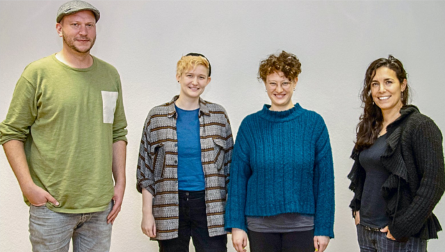 Vier Personen stehen in einer Reihe und lächeln in die Kamera