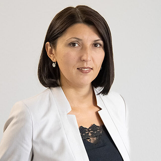 Frau mit schwarzen Haaren und weißem Blazer vor weißem Hintergrund