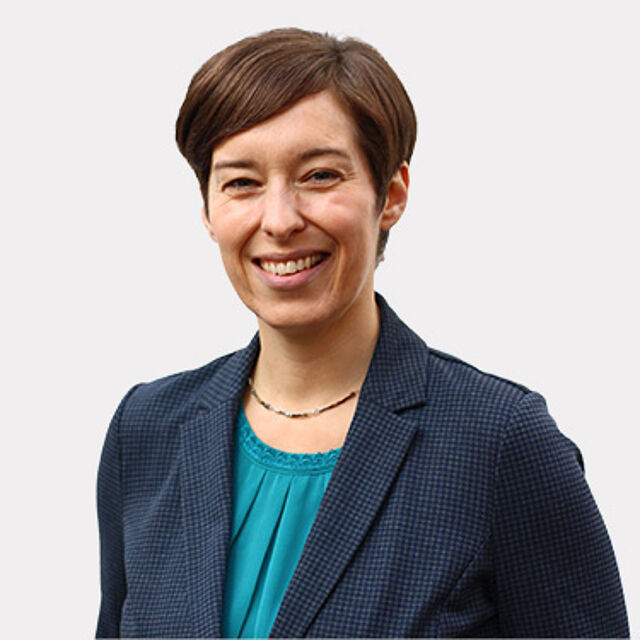 Frau mit kurzen braunen Haaren, blauem Oberteil und Blazer vor weißem Hintergrund
