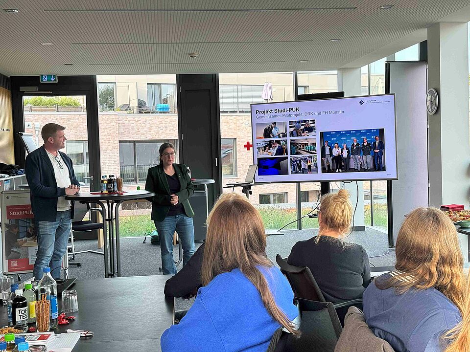 Auftakt StudiPUK Zwei Personen halten eine Präsentation, die auf einem Bildschirm zu sehen ist, zum Thema "StudiPUK" vor einem Publikum