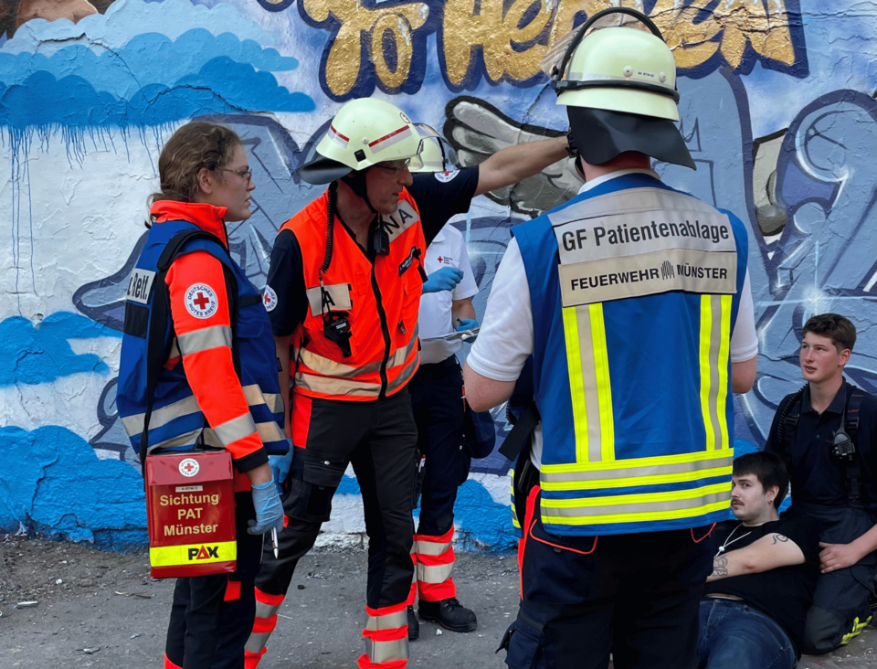 Drei Einsatzkräfte vor einer Graffitwand, im Hintergrund zwei Personen auf dem Boden