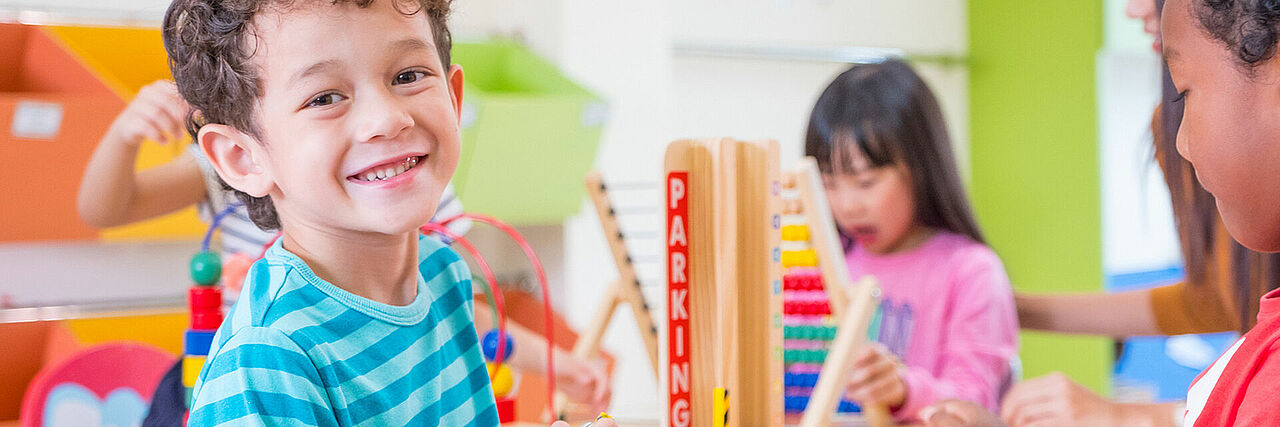 Kita Slider Mehrere Kinder spielen mit Spielzeugen, ein Kind im Vordergrund, der Rest unscharf im Hintergrund