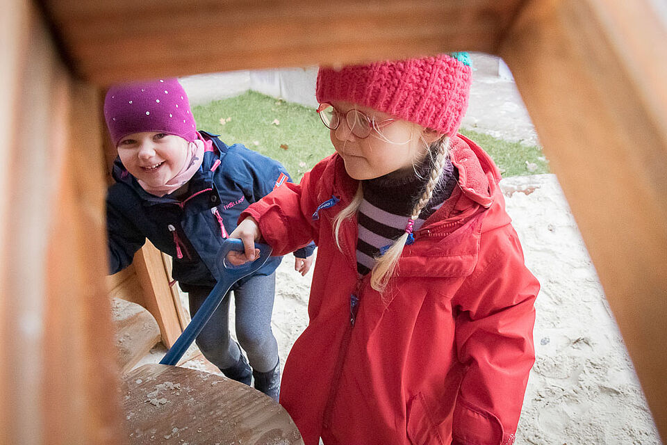 Zwei Kinder in warmer Kleidung befinden sich unter einem Klettergerüst