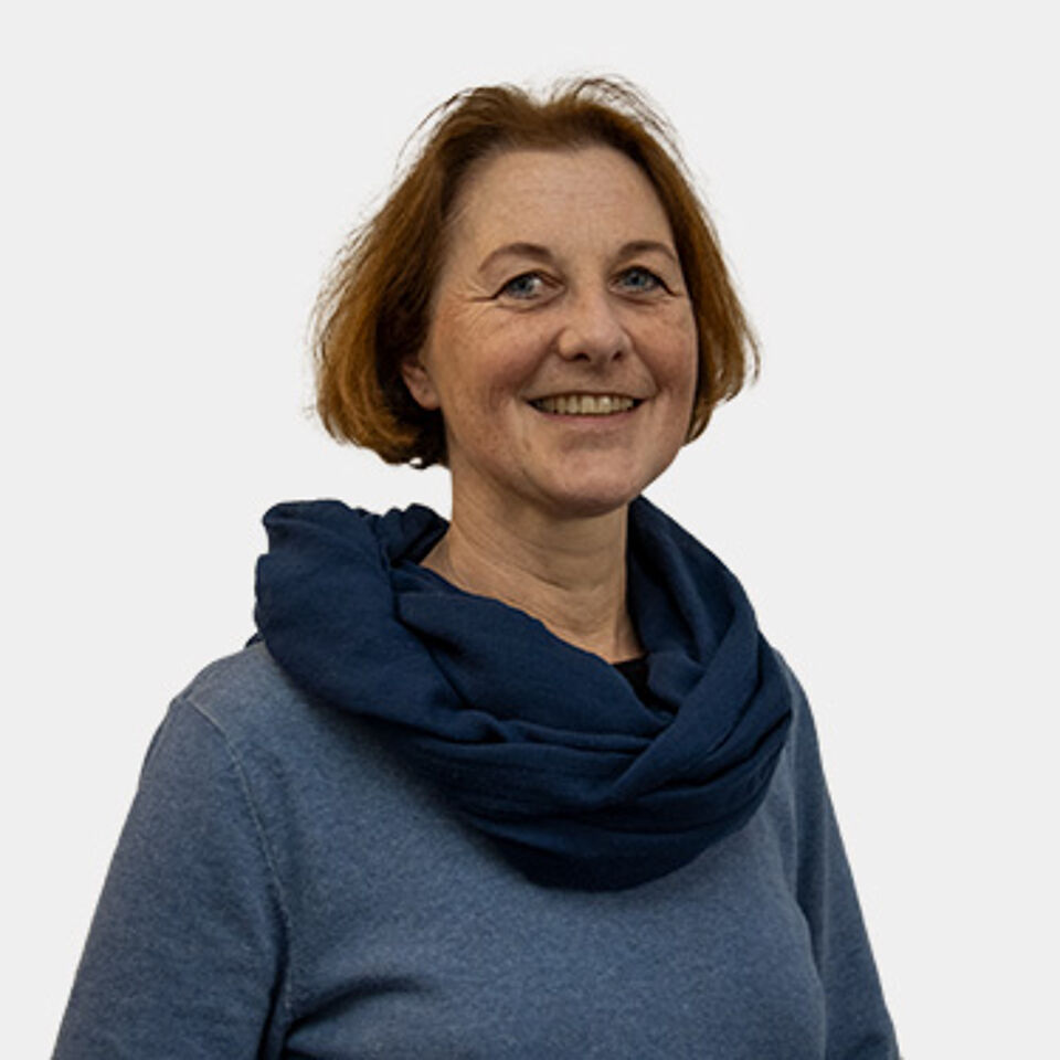 Frau mit braunen Haaren, blauem Schal und blauem Pullover vor weißem Hintergrund
