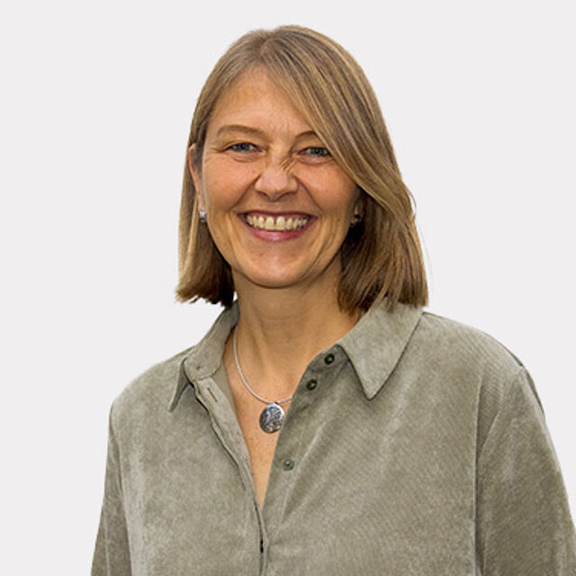 Frau mit blonden Haaren und einem grauen Hemd vor einem weißen Hintergrund