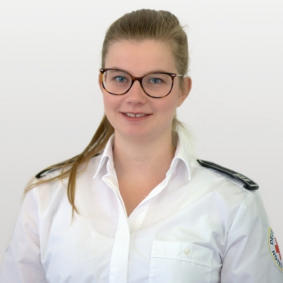 Frau mit blonden Haaren und Brille in einem weißen Hemd mit DRK-Logo und Schulterklappen vor weißem Hintergrund