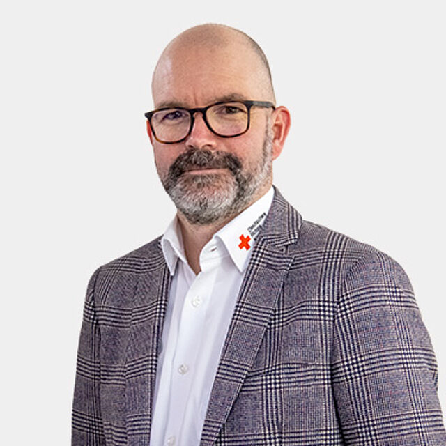 Mann mit Brille und weißem DRK-Hemd und gemustertem Sakko