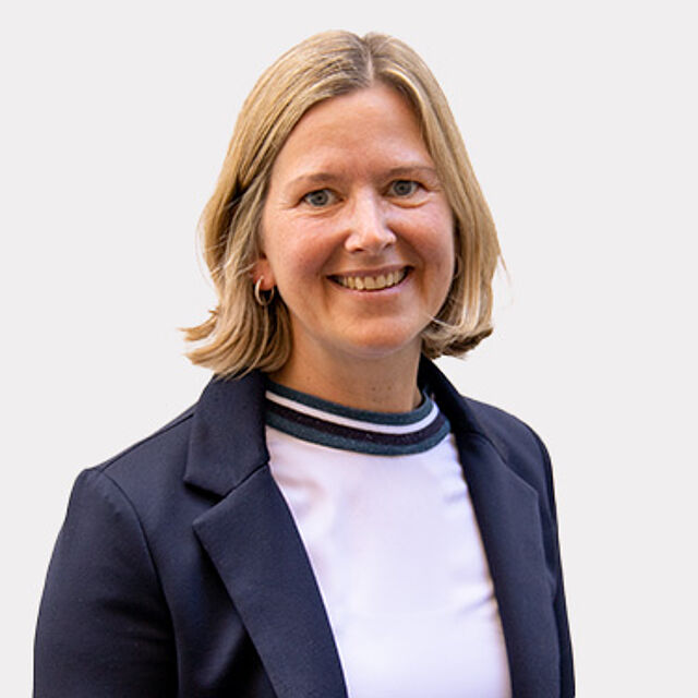 Frau mit blonden Haaren, Blazer und weißem Oberteil vor weißem Hintergrund