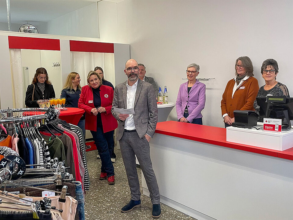 Eröffnung Kleiderladen Vorstand Ein Mann mit Brille in einem karierten Anzug begrüßt die Gäste