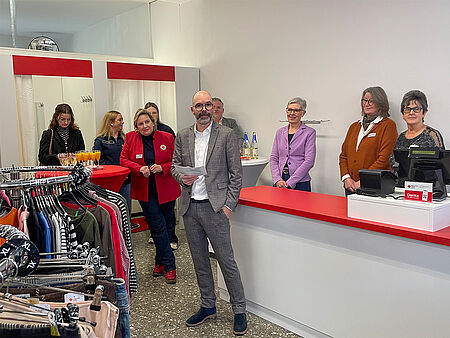 Eröffnung Kleiderladen Vorstand Ein Mann mit Brille in einem karierten Anzug begrüßt die Gäste