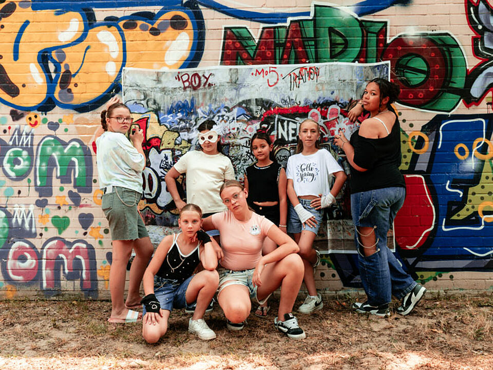Sieben Mädchen vor einer Wand mit Graffiti