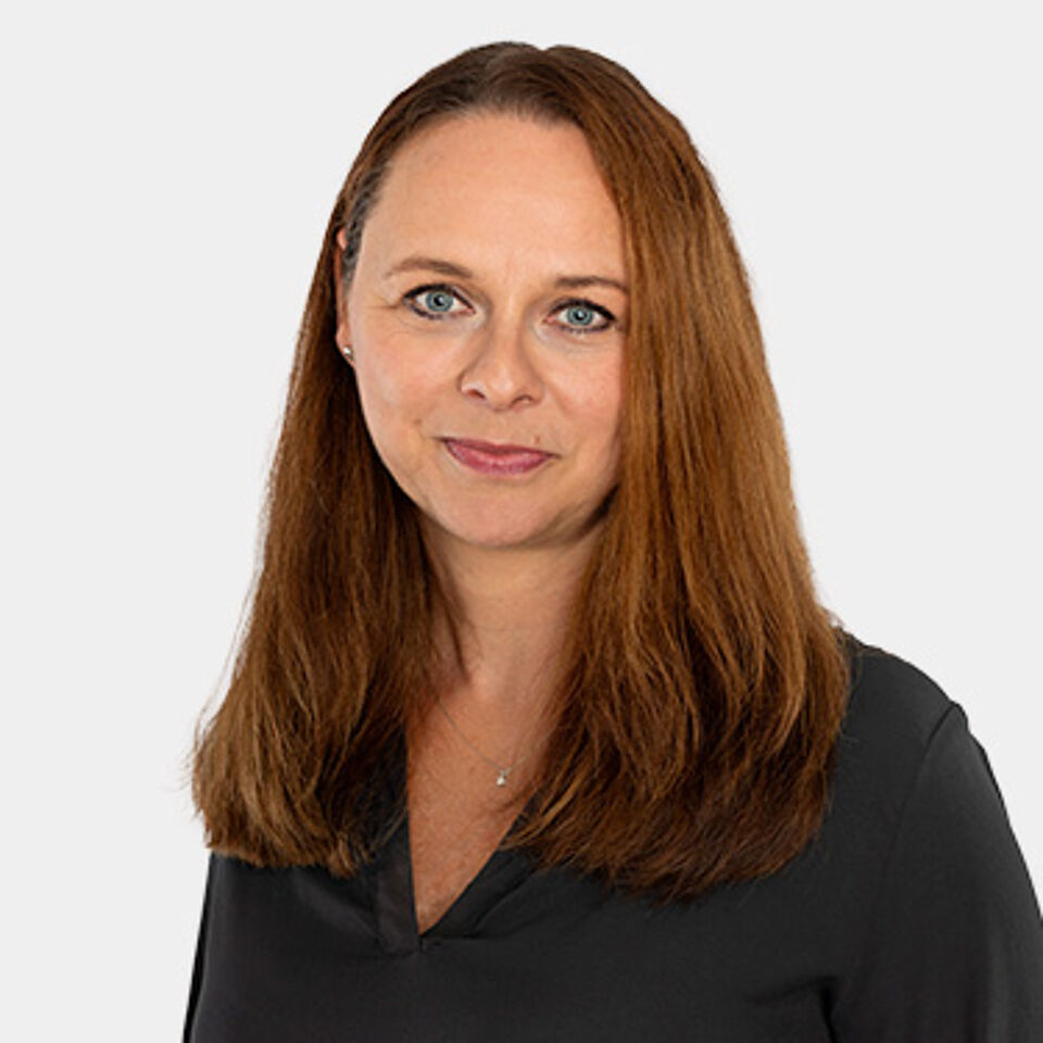 Frau mit braunen Haaren und schwarzem Oberteil vor weißem Hintergrund