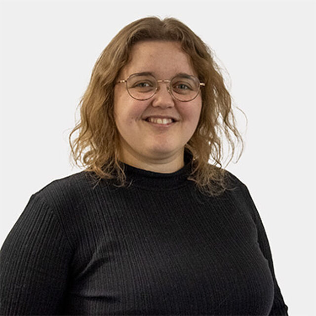 Frau mit blonden Haaren, Brille und schwarzem Oberteil vor weißem Hintergrund
