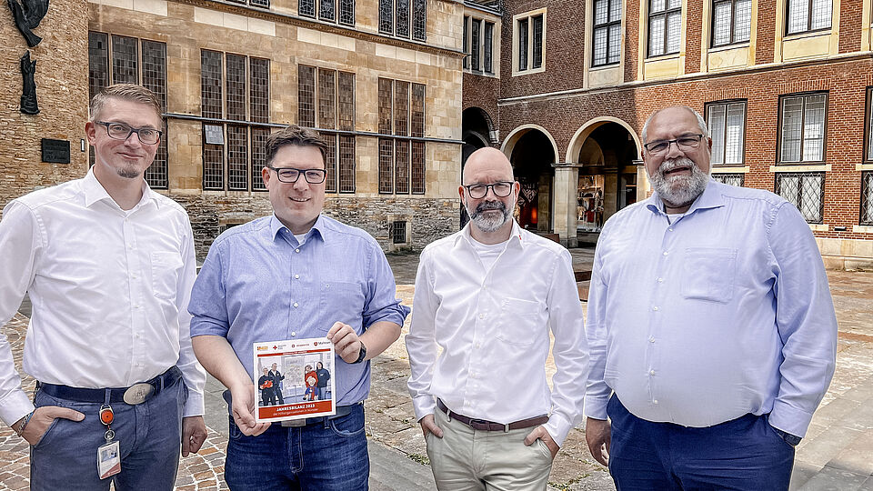 Vier Männer stehen in einem historischen Innenhof und präsentieren eine Broschüre