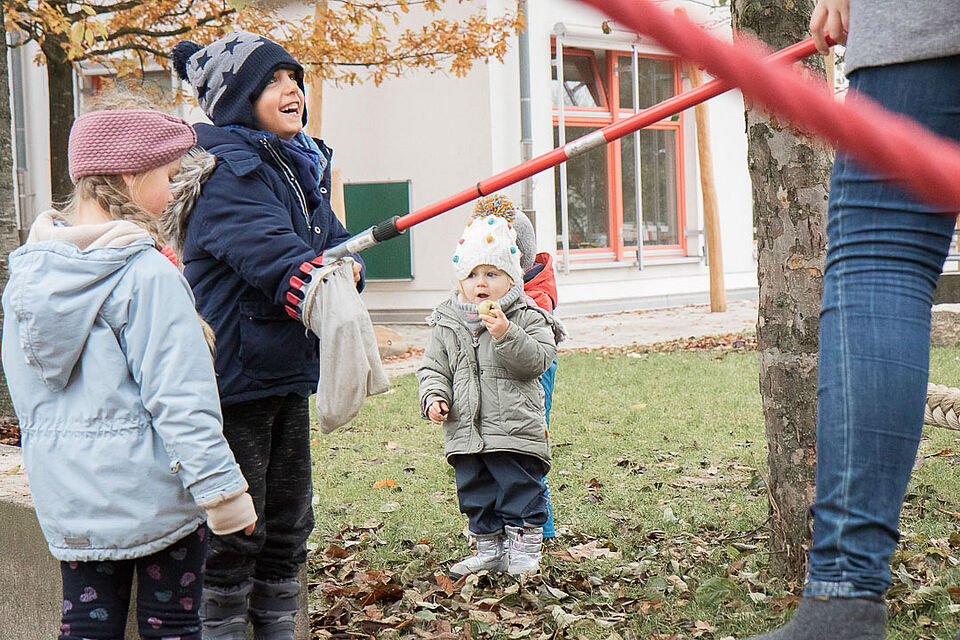 Kinder in warmer Kleidung stehen neben mit einem Apfelpflücker neben einem Baum