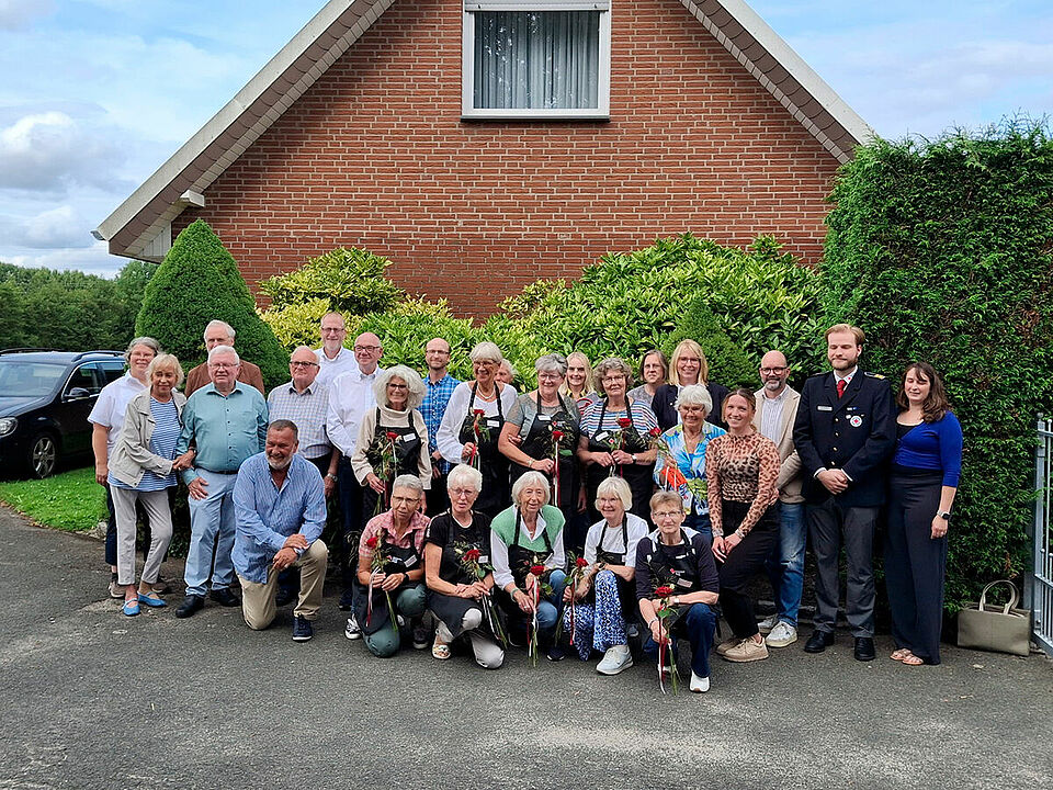 Gruppenfoto Eine Gruppe von Personen steht vor einer grünen Hecke, im Hintergrund ist ein Haus zu sehen.