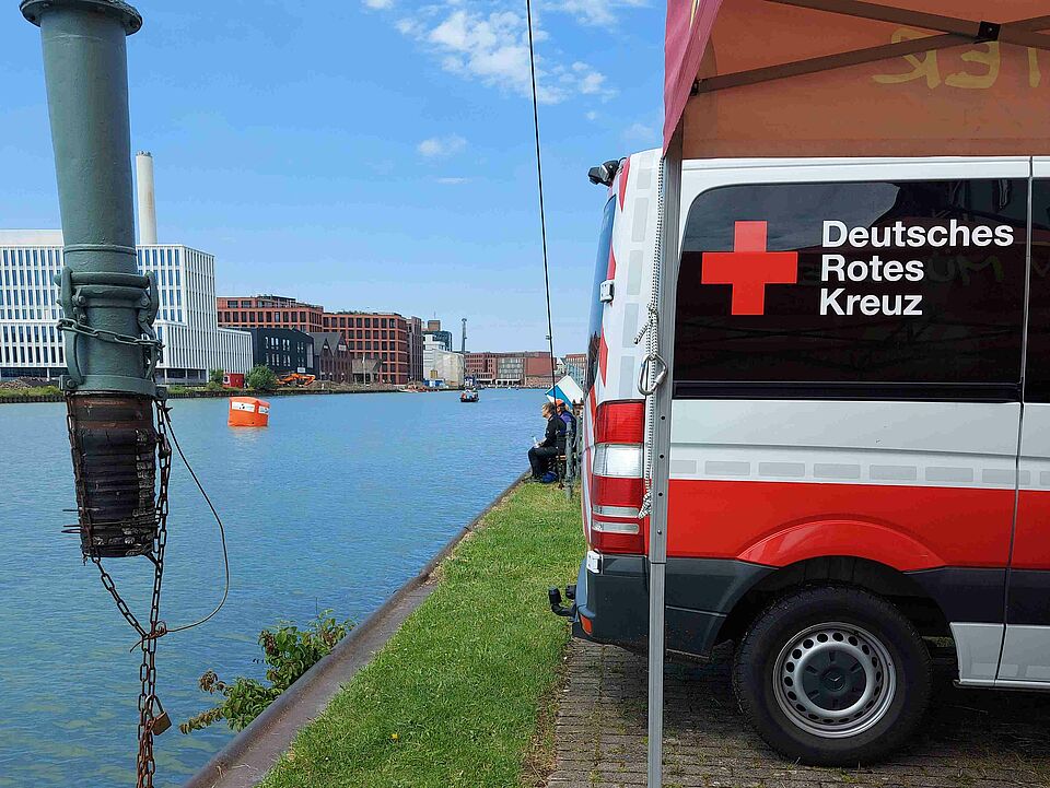 Hafen Kanal mit Häusern im Hintergrund. Im Vordergrund Einsatzfahrzeug mit DRK-Logo