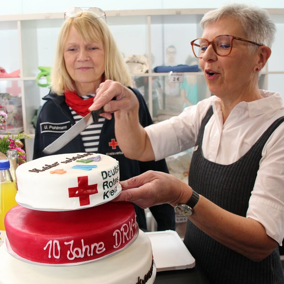 10 Jahre Kleiderladen Zwei Frauen schneiden eine Torte mit dem Schriftzug "10 Jahre Kleiderladen" und einem Rotkreuzlogo an