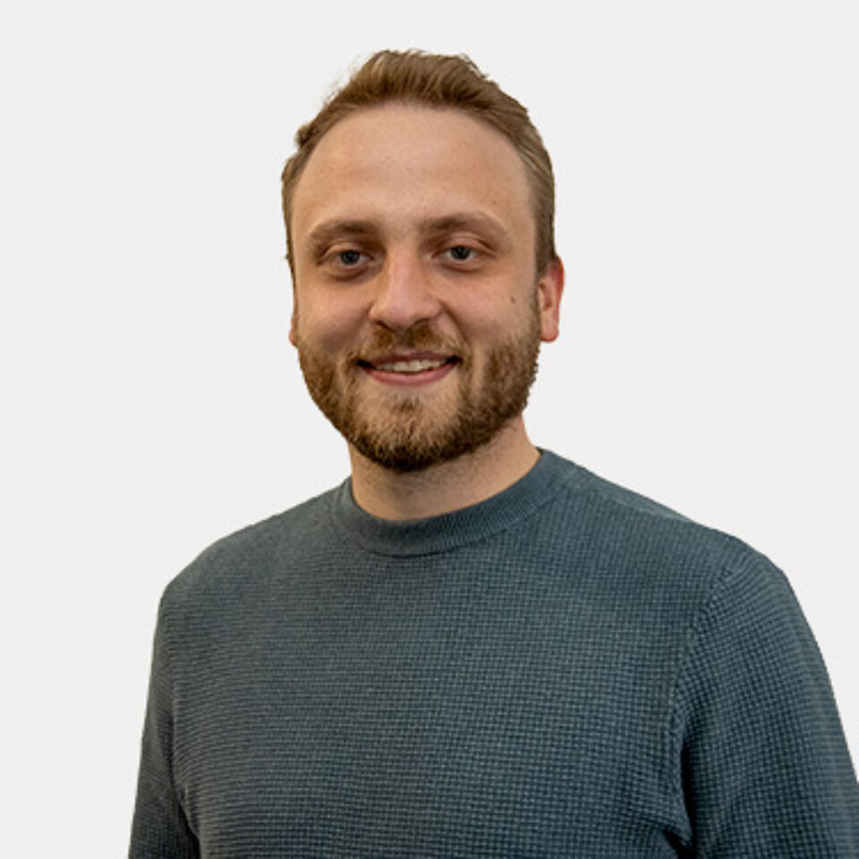 Mann mit blonden Haaren und grauem Pullover vor weißem Hintergrund