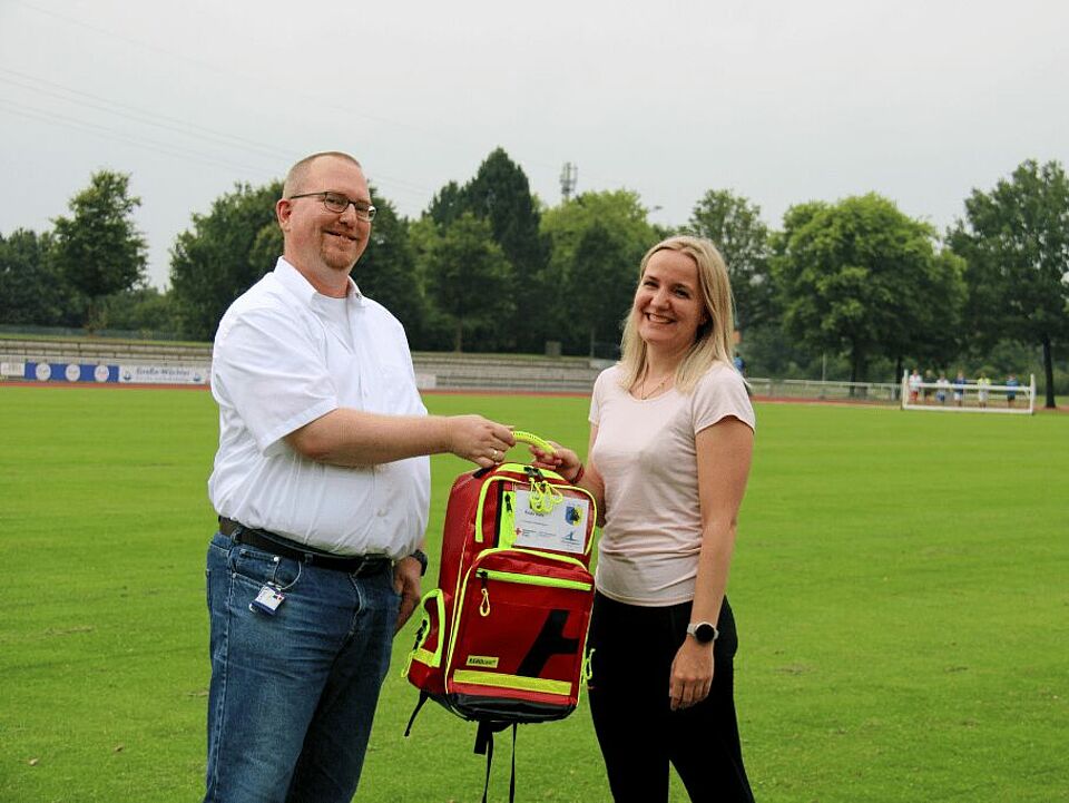 Übergabe Rucksack Eine Person übergibt einer anderen Person einen Notfallrucksack auf einem Sportplatz.