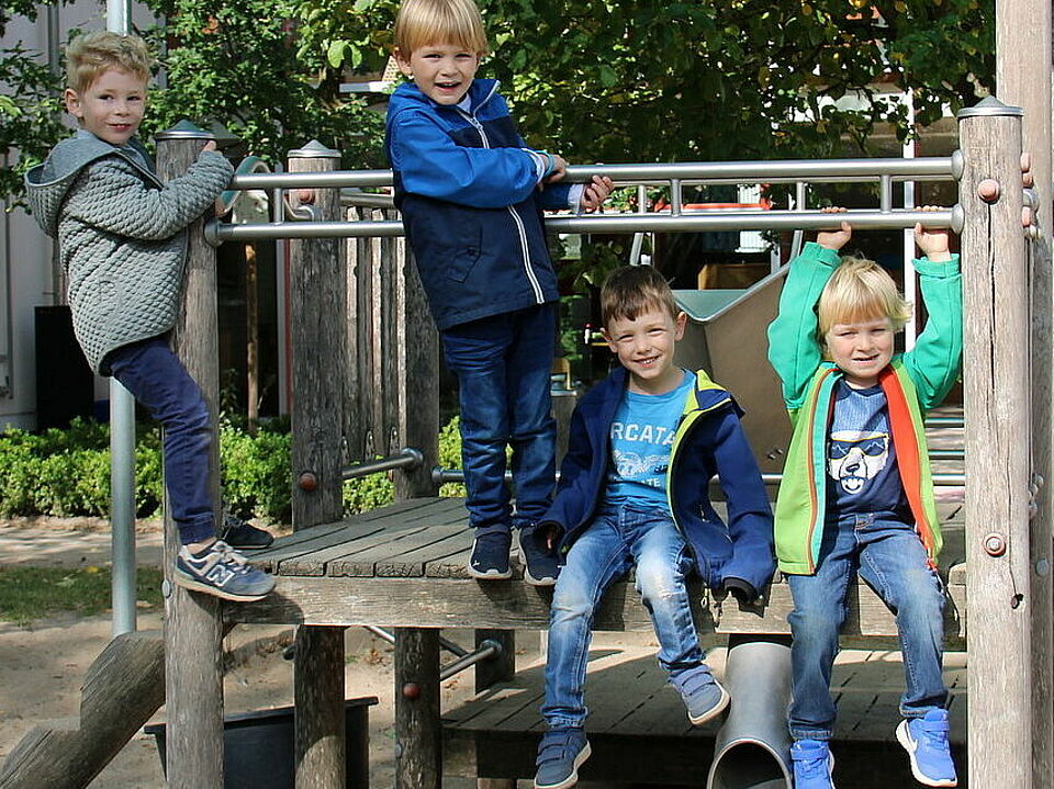 Vier Kinder auf einem Klettergerüst, im Hintergrund ein Gebäude