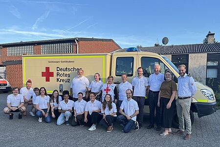 Eine Gruppe von Personen in Rotkreuzeinsatzkleidung steht vor einem Gerätewagen Sanitätsdienst