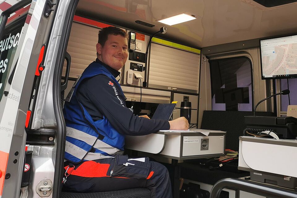 Rosenmontag ELW Person mit Einsatzkleidung und blauer Weste sitzt im Einsatleitungswagen am Laptop.