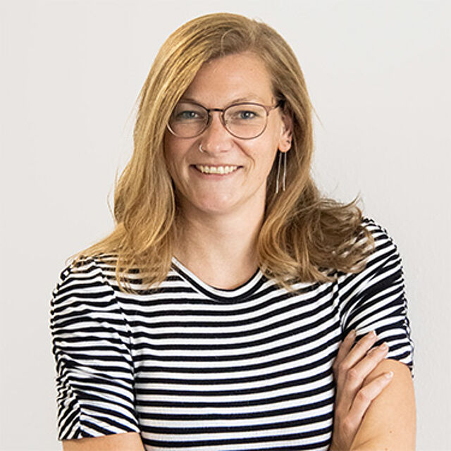 Frau mit blonden Haaren, Brille und gestreiftem Oberteil vor weißem Hintergrund