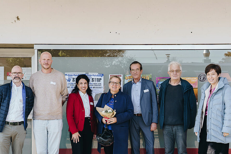 Besuch Svenja Schulze Sieben Personen stehen vor einem Fenster mit Plakaten, eine Person hält einen Blumenstrauß.