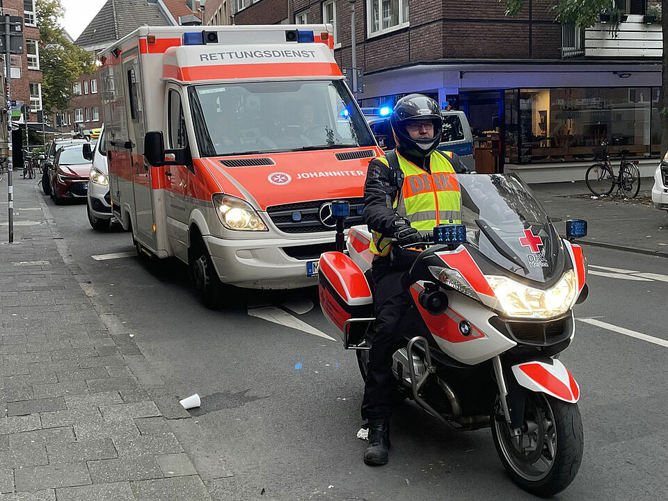 Giro 2025 Ein Motorrad des DRK Herten mit einer Person in Einsatzkleidung, im Hintergrund ein Rettungswagen der Johanniter