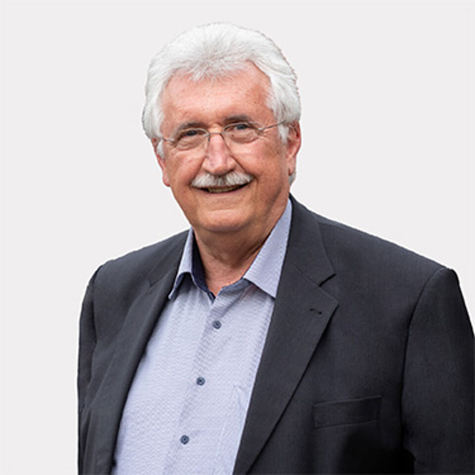 Mann mit Brille, blauem Hemd und schwarzem Sakko vor weißem Hintergrund