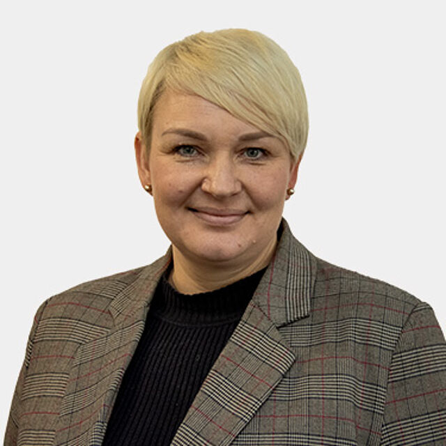 Frau mit kurzen blonden Haaren, schwarzem Oberteil und braunem Blazer