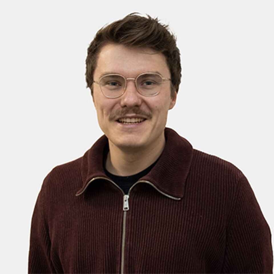 Mann mit braunen Haaren, Brille und braunem Pullover
