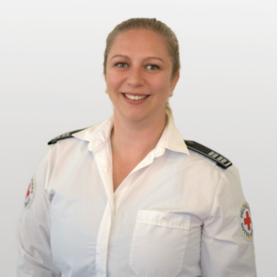 Frau mit blonden Haaren, weißem Hemd mit DRK-Logo und Schulterklappen vor weißem Hintergrund