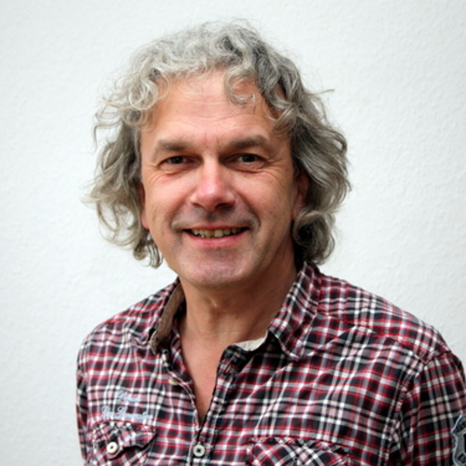 Mann mit grauen Locken und karrierten Hemd vor weißem Hintergrund