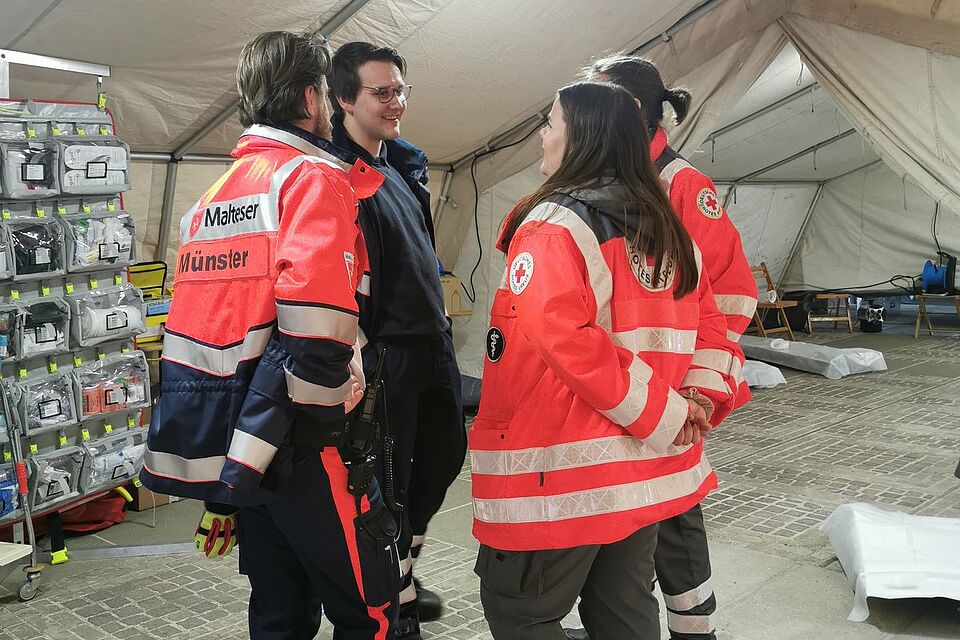 Rosenmotnag Vier Personen in Einsatzkleidung verchiedener Hilfsorganisationen stehen in einem Zelt in einem Kreis zusammen