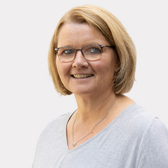 Frau mit blonden Haaren und Brille mit grauem Oberteil vor weißem Hintergrund