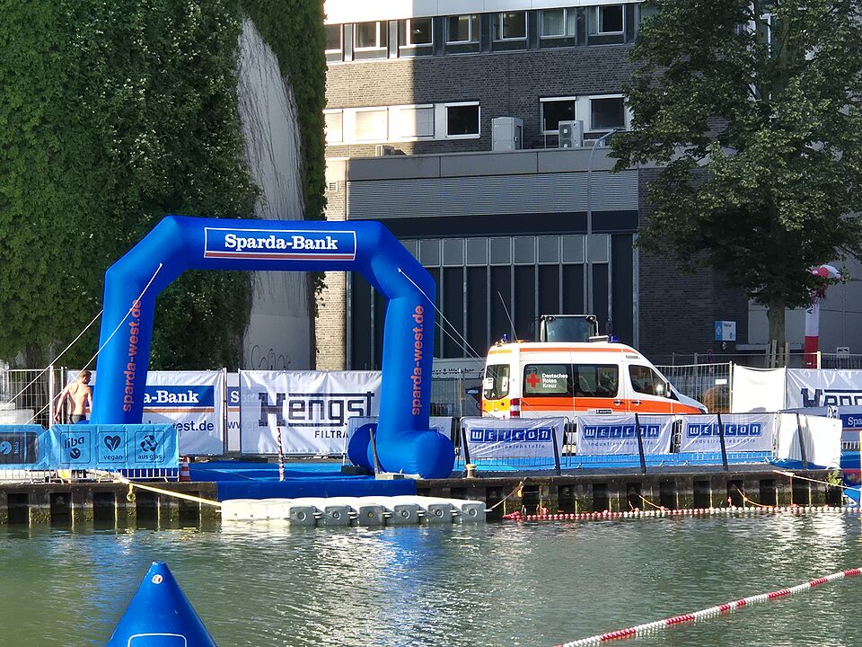 Schwimmausstieg des Triathlons am Hafen mit blauem Sparda-Bank Luftbogen und KTW im Hintergrund
