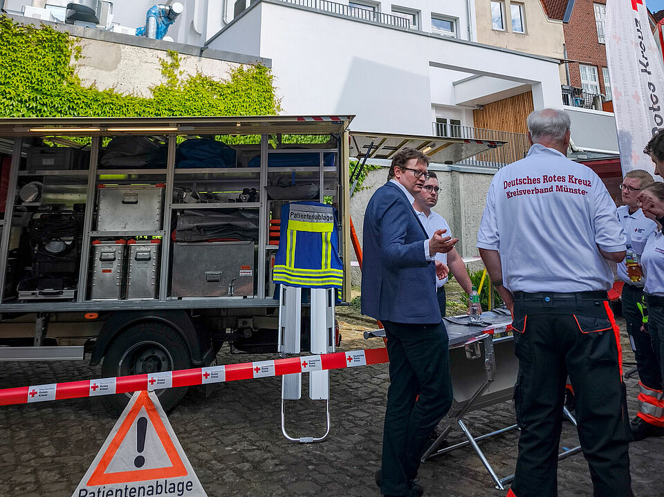 Ein Gerätewagen mit Menschen, teilweise in Einsatzkleidung, davor im Gespräch. Im Hintergrund die Lambertikirche.