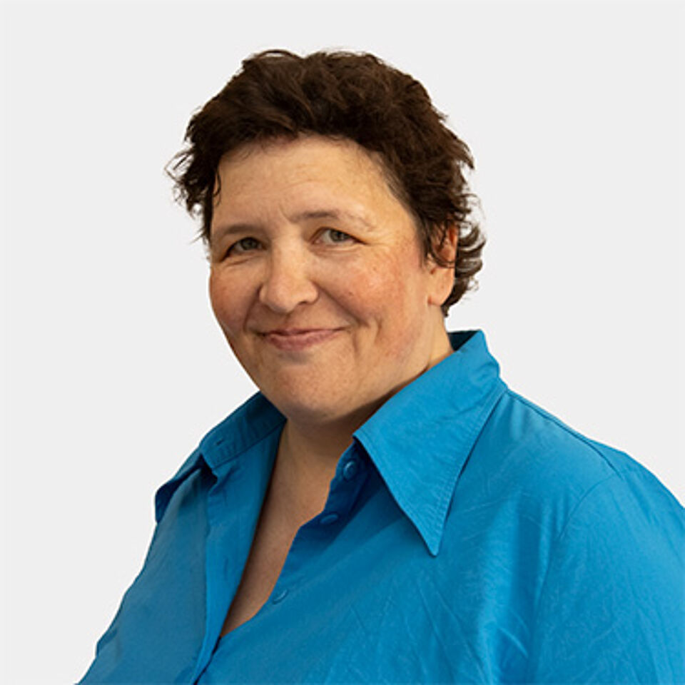 Frau mit kurzen braunen Haaren und blauer Bluse vor weißem Hintergrund