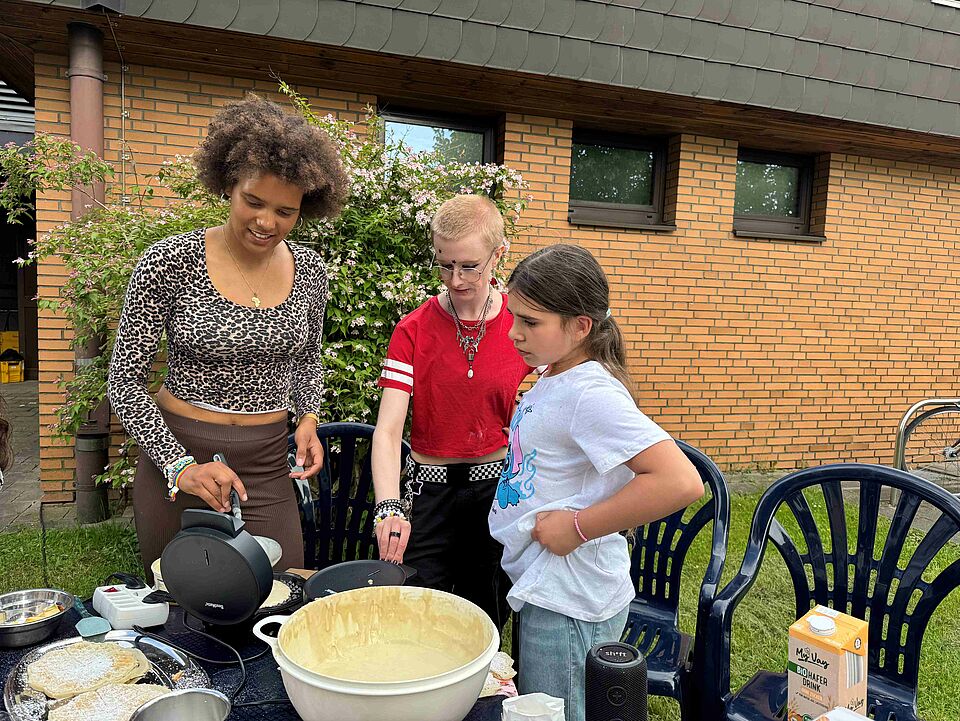 Drei Personen stehen an einem Tisch und backen Waffeln